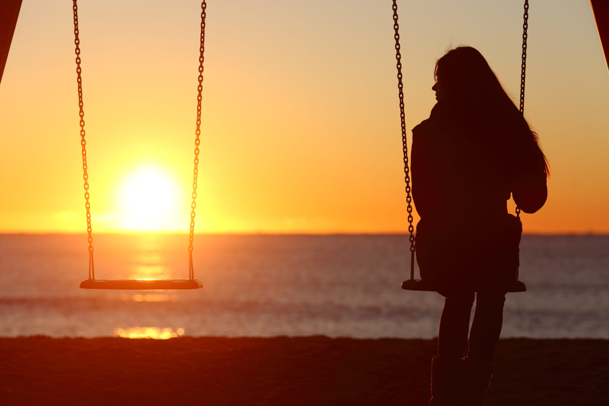 Single woman on swingset with sunset